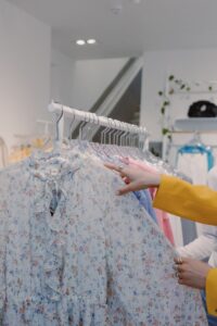 Woman browsing floral print dresses on a clothing rack indoors in a fashion store.